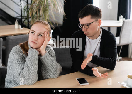 Agacé homme essayant d'expliquer quelque chose à sa femme assis sur un canapé dans le café Banque D'Images