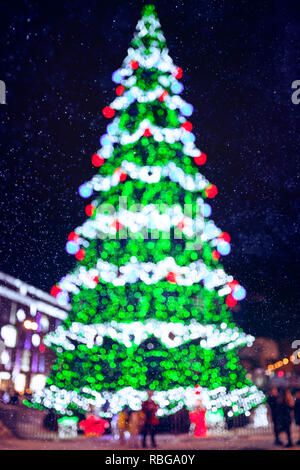 Flou artistique en couleur des lumières d'arbre de Noël sur fond de ville et de la neige dans la nuit Banque D'Images