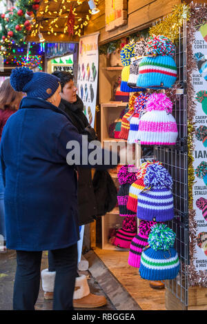 Personnes (femmes) au marché de Noël (clients potentiels) à une variété de chapeaux colorés bobble laineux sur l'affichage - York, England, GB, UK Banque D'Images