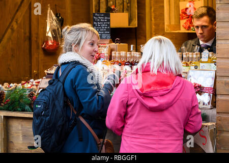 Homme travaillant à la vente de boissons liqueurs de fruits et les clients potentiels (les femmes de l'échantillon de l'EPLA) profitant des boissons - Marché de Noël de New York, England, UK. Banque D'Images