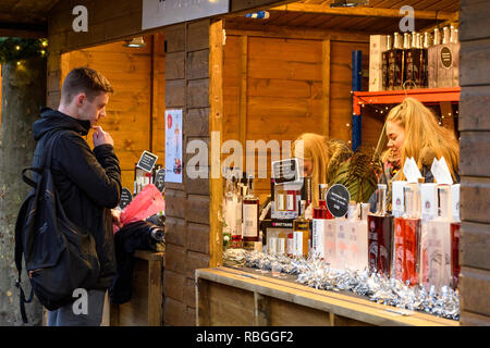 Les personnes qui travaillent à la vente de la vodka gin & Brittain & client potentiel au marché de Noël à la recherche de liste de prix sur écran - York, England, UK. Banque D'Images