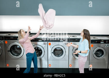 Les jeunes femmes espiègles et jeter vers le haut d'une serviette après le lavage des vêtements à la blanchisserie publique Banque D'Images