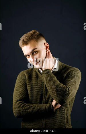 Portrait of young man wearing green pull debout sur le fond gris et tenant son cou au studio Banque D'Images