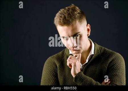 Portrait de jeune homme portant beau grave pull vert debout sur le fond gris et poising au studio Banque D'Images