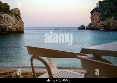 Des chaises en plastique et une table face à l'océan. Loin d'un coup petit bateau au milieu et deux rochers debout sur l'eau bleu cristal. Destination de voyage Banque D'Images