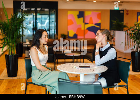 Deux jeunes femmes ont une réunion ensemble dans un bureau pendant la journée. Ils sont d'une équipe diversifiée, l'un est de race blanche, l'autre chinois. Banque D'Images
