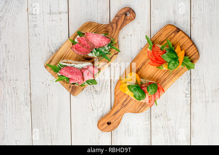 Variété de mini sandwiches au fromage à la crème, légumes et de salami. Des sandwichs au fromage, salami, tomate, basilic, sur un fond clair, vue du dessus. Mise à plat Banque D'Images