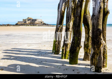 Le Fort National, construit au large de la côte de Saint-Malo en Bretagne, vu de la plage à marée basse avec brise-lames en bois posts au premier plan. Banque D'Images