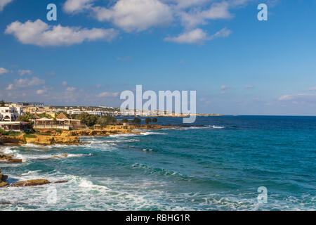 Vue de l'ouest à la côte vers le bas le petit village (Limenas Chersonisou) sur l'île de Crète en Grèce, avec un ciel bleu avec quelques nuages. Banque D'Images