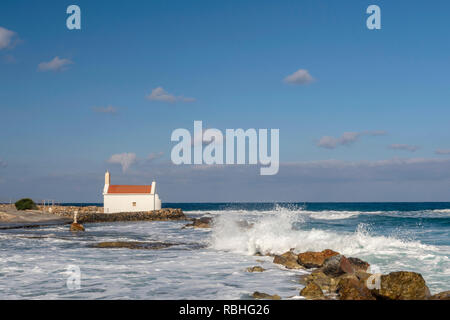 Peu d'église de Marin (Agios Nikolaos) avec la mer bleue et les vagues et un ciel bleu en arrière-plan, photo de l'île de Crète en Grèce. Banque D'Images
