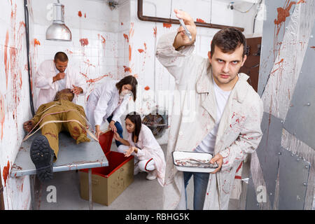 Guy s'amusant avec des amis en quête prix en chambre chirurgicale avec des traces de sang, effrayant avec des instruments médicaux sur l'appareil photo Banque D'Images