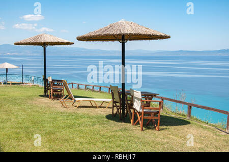 Fournir de l'ombre des parasols en chaume pour les tables et chaises donnant sur le golfe Kassandras à Halkidiki, Grèce Banque D'Images