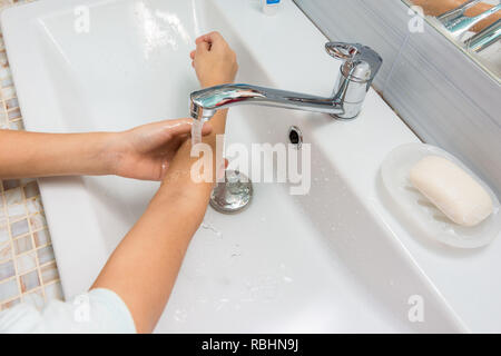 L'enfant se lave les mains jusqu'aux coudes dans le lavabo de la salle de bains Banque D'Images