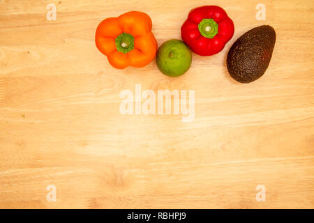 Légumes colorés : Deux poivrons, une lime et un avocat assis sur une table de cuisine. Banque D'Images