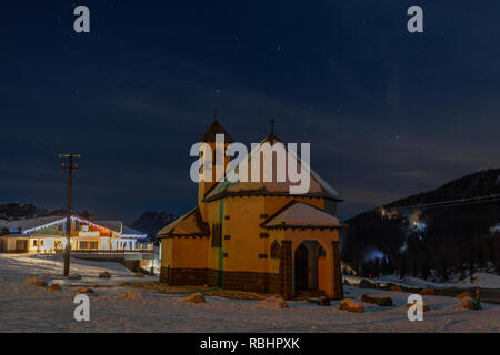 Vue de nuit sur une petite église du San Pellegrino Pass en hiver, avec les pistes de ski en arrière-plan, Dolomites, Italie Banque D'Images