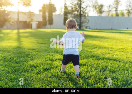 Mignon bébé fonctionne sur une pelouse verte en rattrapage, dans la nature sur une journée ensoleillée. Le concept de un an et les premiers pas de l'enfant