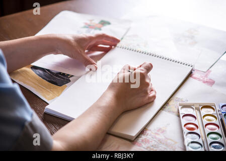 Les belles mains, peindre avec un pinceau aquarelle du gâteau sur une feuille de papier blanc. Banque D'Images