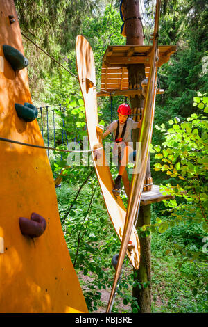 Adolescents le port du harnais de sécurité pont de corde passant à un obstacle au parcours aventure accrobranche de plein air park Banque D'Images