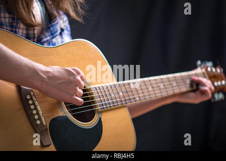 La jeune fille jouant une guitare acoustique sur un fond sombre dans le studio. Les concerts de jeunes musiciens Banque D'Images