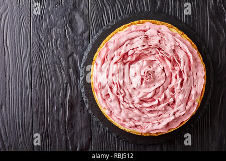 Cheesecake framboise garni de fromage à la crème avec motif couleur framboises sur une pierre noire sur le plateau de table en bois, flatlay, copy space, close-up Banque D'Images