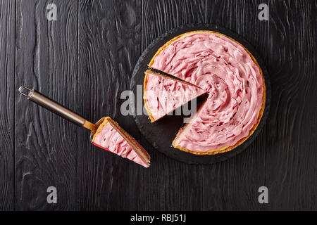 Cheesecake framboise garni de fromage à la crème de couleur avec les framboises au sol sur une pierre noire en tranches sur le plateau de table en bois, vue de dessus, close-up Banque D'Images