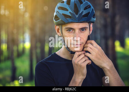 Cycliste homme porte un casque gris sport sur sa tête dans l'arrière-plan de la nature verte. Le concept de protection obligatoire au cours de Vélo Banque D'Images