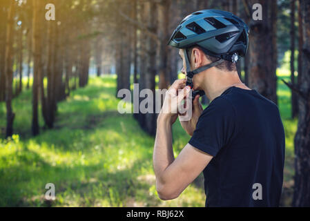 Cycliste homme porte un casque gris sport sur sa tête dans l'arrière-plan de la nature verte. Le concept de protection obligatoire au cours de Vélo Banque D'Images