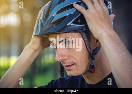 Cycliste homme porte un casque gris sport sur sa tête dans l'arrière-plan de la nature verte. Le concept de protection obligatoire au cours de Vélo Banque D'Images