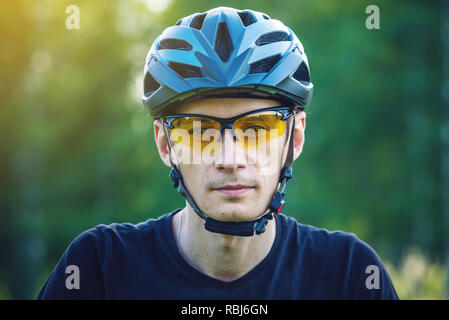 Cycliste homme porte un casque gris sport sur sa tête dans l'arrière-plan de la nature verte. Le concept de protection obligatoire au cours de Vélo Banque D'Images