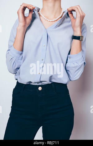 Jeune femme élégante vêtue de jeans skinny noir, chemise bleue et pearl collier posing holding collier avec les deux mains. Banque D'Images