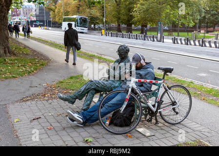 Un homme assis sur un banc à côté d'une stature et la lecture d'un livre par le Grand Canal navigable à Dublin, Irlande. Banque D'Images