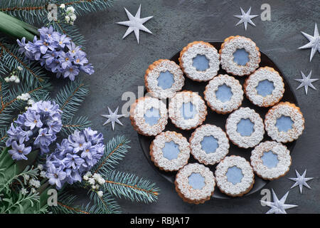 Vue de dessus de fleur bleue linzer cookies sur fond vert foncé en hiver sapin décoré avec des brindilles, des fleurs de jacinthe bleu, pommes de pin et des étoiles Banque D'Images