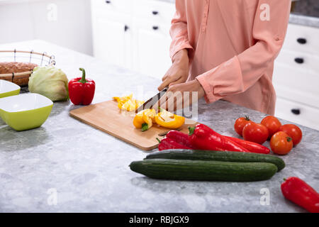 Woman Chopping Bell Pepper sur planche à découper avec couteau sur le comptoir de la cuisine Banque D'Images