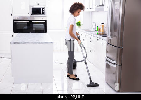Close-up of a young woman nettoyage du plancher de la Cuisine blanche avec aspirateur Banque D'Images