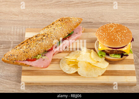 Ciabatta frais sandwich avec jambon de porc et légumes, délicieux cheeseburger et croustilles de pommes de terre sur une planche à découper en bois Banque D'Images