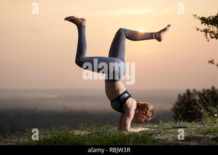 Profil des pieds nus musculaire solide girl doing difficile compliqué les exercices de yoga en plein air, sur fond de pré herbeux sur ciel d'été et blurre Banque D'Images