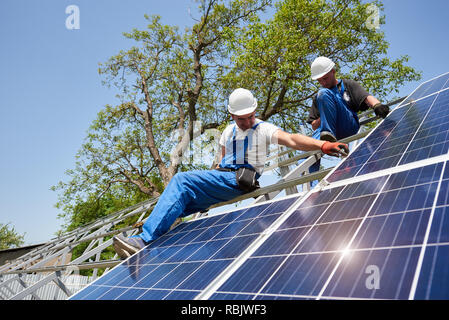 Deux techniciens sur la plate-forme de métal haute contre ciel bleu et l'arbre vert travaille sur l'installation du système de panneaux solaires photovoltaïques. Écologique renouvelable Banque D'Images