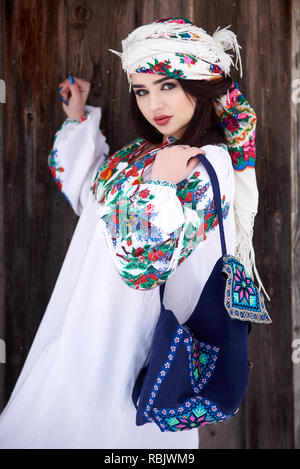 Les jeunes à la mode attrayant femme brune en robe blanche, manches brodé de fleurs colorées, fichu et bleu , sac épaule o Banque D'Images