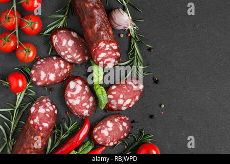 Salami en tranches avec les tomates, le romarin et le poivre noir sur fond d'ardoise. Salami saucisse. top view with copy space Banque D'Images