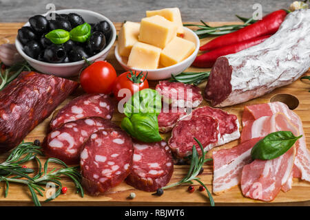 Tranches de salami, bacon, saucisses, fromage, olives, tomates et fines herbes. Plateau d'antipasto de viande sur la table en bois. close up Banque D'Images