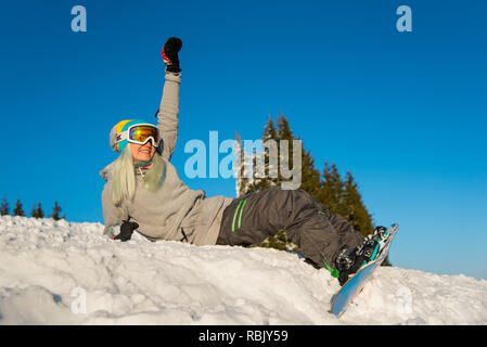 Low angle view of a happy girl snowboarder assis sur le dessus de la pente, de sourire et de détente en plein air sur la neige sur une belle soirée d'hiver ensoleillé Banque D'Images