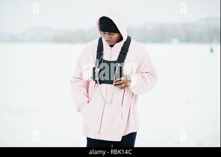 Style urbain élégant african american man en rose hoodie posés au lac gelé en hiver. Banque D'Images