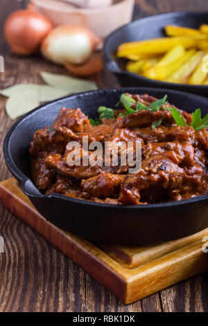 Bœuf Stroganoff à la sauce tomate et la crème sure et de pommes de terre frits servis dans la poêle en fonte sur table en bois rustique Banque D'Images