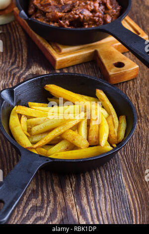 Poêlée de pommes de terre et boeuf stroganoff avec de la sauce tomate et la crème fraîche dans la poêle en fonte sur table en bois rustique Banque D'Images