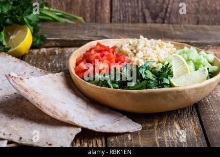 Taboulé de boulgour, saladier avec du persil frais, tomates, concombres, servi avec pain pita sur table en bois rustique, portrait, close-up Banque D'Images