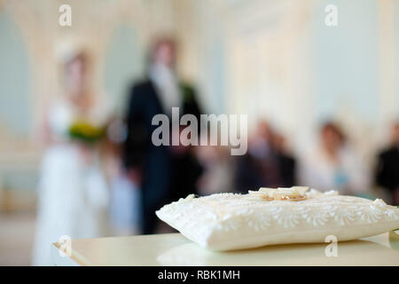 Une paire de bagues de mariage sur un oreiller blanc. Dans l'arrière-plan flou sont des silhouettes de la mariée et le marié. Banque D'Images