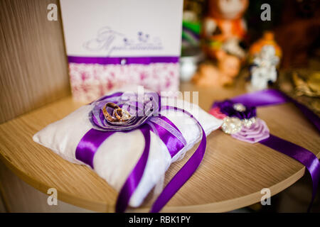 Une paire de bagues de mariage se coucher sur un oreiller blanc avec des rubans violets. Dans l'arrière-plan flou dans la carte postale et distinguer les jouets. Banque D'Images