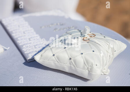 Une paire de bagues de mariage sur un oreiller blanc. Joints toriques liés ruban blanc. Banque D'Images