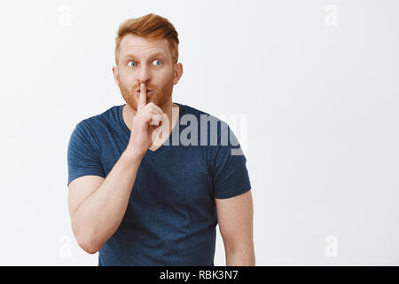 Jolie rousse nerveux avec guy beard, flexion vers la caméra montrant chut chut, disant geste avec l'index sur la bouche, regardant anxieusement à droite, en gardant le secret, les rumeurs disent Banque D'Images