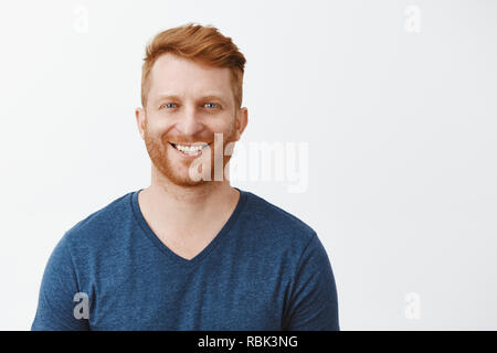 Taille plan sur charmante rouquine mature homme européen avec des pinceaux en soie naturelle et de beaux yeux bleus debout au-dessus de mur gris en bleu t-shirt, souriant joyeusement, avoir la conversation et profiter de grand jour Banque D'Images